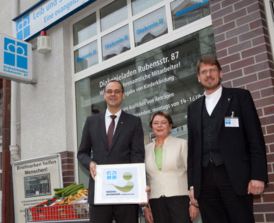 Oliver Pöpplau, Vorstand der PSD Bank, Magrit Knapp,   Friedenau-Netzwerk, und Pfarrer Thomas Lübke von der   Philippus-Nathanael-Gemeinde (v.l.) vor dem Diakonieladen in der   Rubensstraße